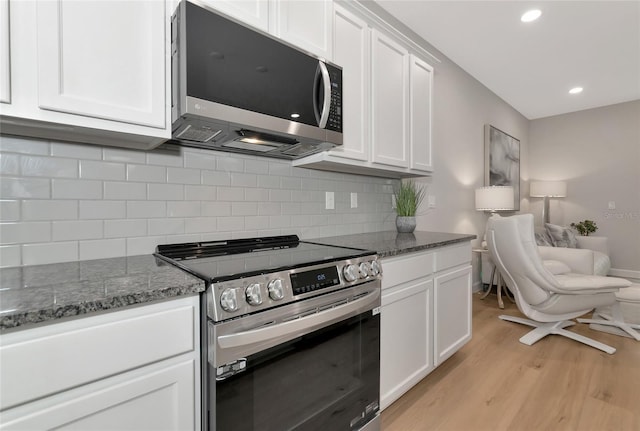 kitchen with white cabinetry, light hardwood / wood-style flooring, dark stone countertops, appliances with stainless steel finishes, and decorative backsplash