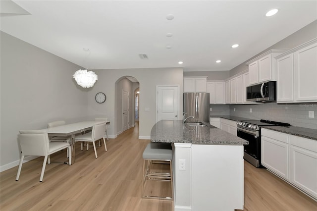 kitchen with appliances with stainless steel finishes, decorative light fixtures, sink, decorative backsplash, and a center island with sink