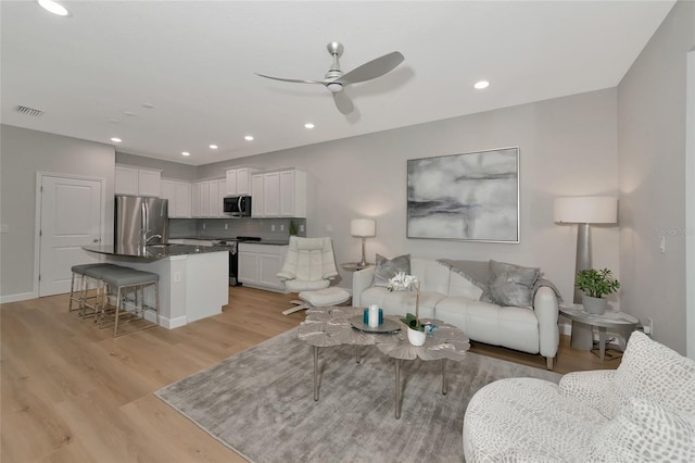 living room featuring sink, ceiling fan, and light wood-type flooring