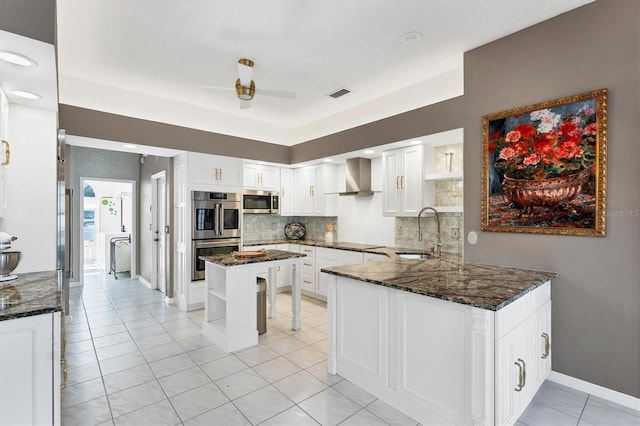 kitchen with appliances with stainless steel finishes, sink, white cabinets, kitchen peninsula, and wall chimney exhaust hood