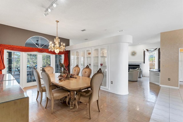 dining space featuring rail lighting, a textured ceiling, a notable chandelier, light parquet flooring, and a fireplace