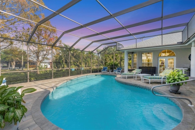 pool at dusk with a lanai, a patio area, and french doors