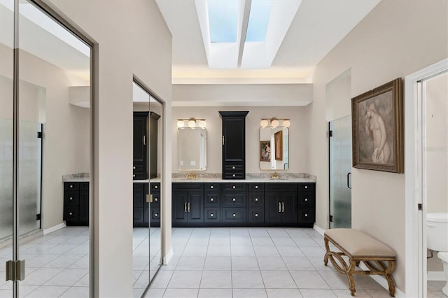 bathroom with a shower with door, a skylight, vanity, tile patterned floors, and toilet