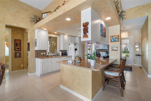 kitchen with white cabinetry, a kitchen bar, white fridge with ice dispenser, light tile patterned flooring, and kitchen peninsula