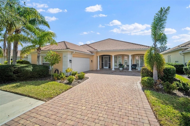 mediterranean / spanish house featuring a garage, a front yard, and covered porch