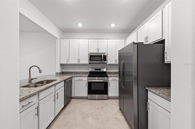 kitchen with sink, appliances with stainless steel finishes, kitchen peninsula, light stone countertops, and white cabinets