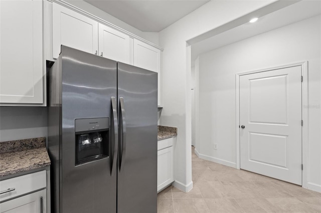 kitchen featuring white cabinetry, stainless steel refrigerator with ice dispenser, light tile patterned flooring, and dark stone counters