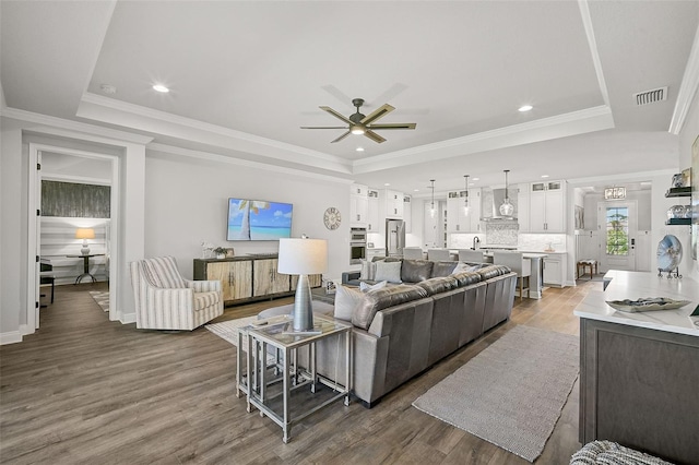 living room with ornamental molding, wood-type flooring, and a tray ceiling