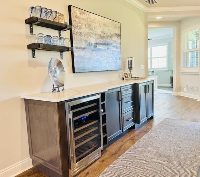 bar featuring wine cooler, crown molding, and hardwood / wood-style floors