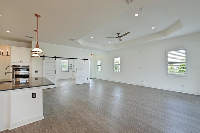 kitchen featuring hanging light fixtures, dark hardwood / wood-style floors, a tray ceiling, white cabinets, and a barn door