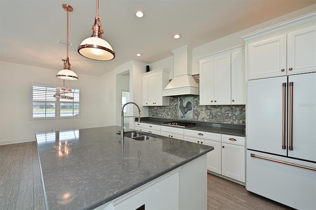 kitchen with sink, custom exhaust hood, paneled built in fridge, pendant lighting, and white cabinets