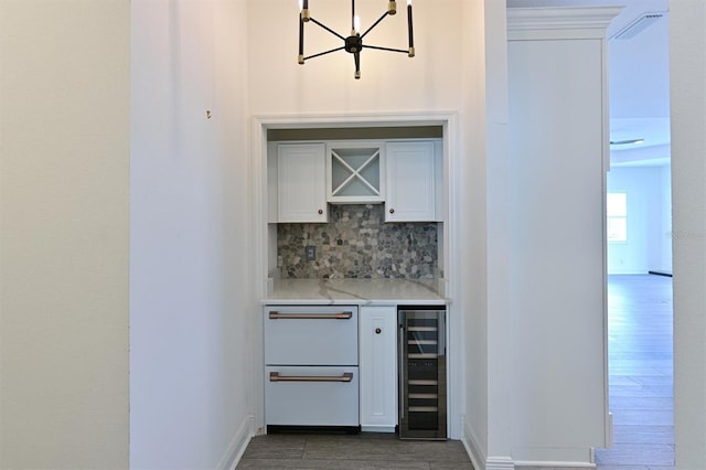 bar featuring hardwood / wood-style flooring, an inviting chandelier, backsplash, white cabinetry, and beverage cooler