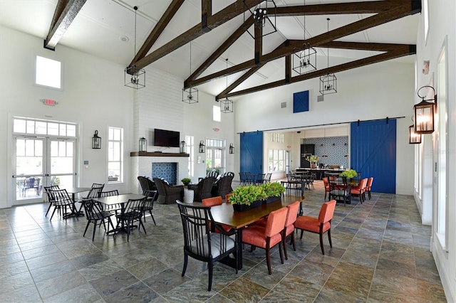 dining space with beamed ceiling, a large fireplace, a barn door, and french doors