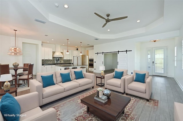 living room with ceiling fan, light hardwood / wood-style flooring, a barn door, and a raised ceiling