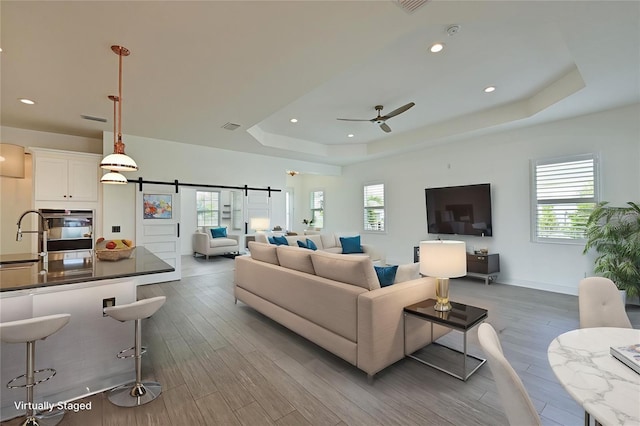 living room featuring wood-type flooring, a wealth of natural light, a barn door, and a raised ceiling