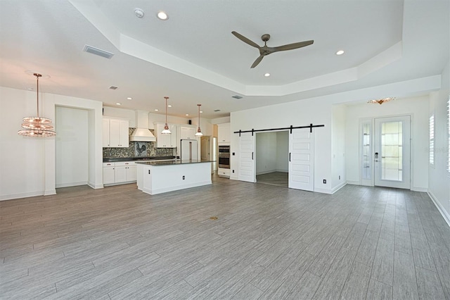 unfurnished living room featuring ceiling fan, a barn door, a raised ceiling, and light hardwood / wood-style flooring