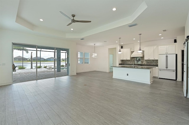 unfurnished living room with sink, ceiling fan, a raised ceiling, a water view, and light hardwood / wood-style flooring