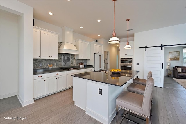 kitchen with pendant lighting, white cabinets, a kitchen bar, a barn door, and custom range hood