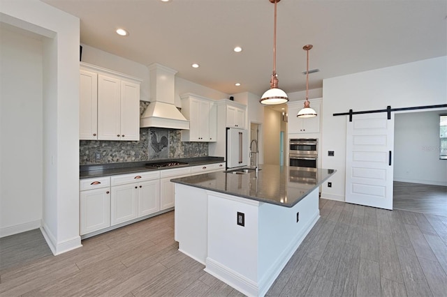 kitchen with custom exhaust hood, a barn door, hanging light fixtures, and white cabinets