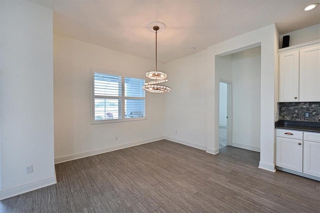 unfurnished dining area featuring a notable chandelier and dark hardwood / wood-style flooring