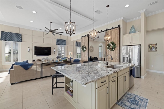 kitchen featuring sink, hanging light fixtures, an island with sink, stainless steel appliances, and cream cabinetry