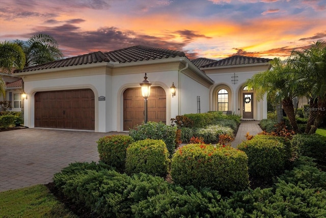 mediterranean / spanish-style home featuring an attached garage, a tile roof, decorative driveway, and stucco siding