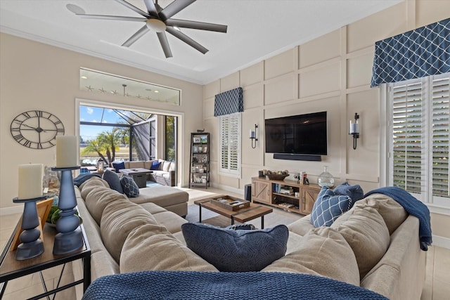 living area featuring light tile patterned floors, baseboards, ceiling fan, crown molding, and a decorative wall