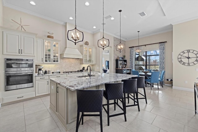 kitchen featuring a breakfast bar area, tasteful backsplash, double oven, a sink, and an island with sink