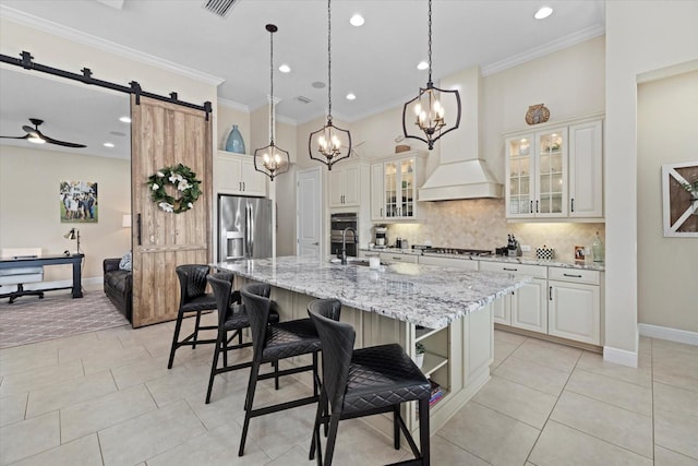 kitchen featuring a barn door, ornamental molding, appliances with stainless steel finishes, backsplash, and a center island with sink