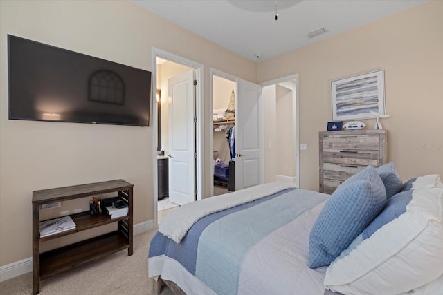 bedroom with connected bathroom, light colored carpet, visible vents, baseboards, and a walk in closet