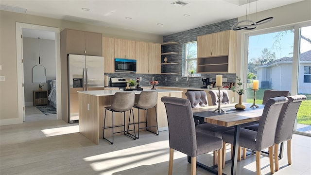 kitchen with pendant lighting, stainless steel appliances, a center island, decorative backsplash, and light brown cabinets