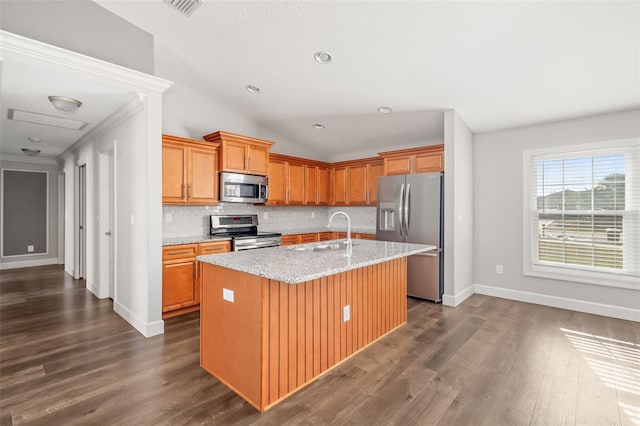 kitchen with sink, appliances with stainless steel finishes, light stone countertops, an island with sink, and decorative backsplash