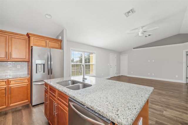 kitchen with lofted ceiling, sink, stainless steel appliances, light stone counters, and a center island with sink