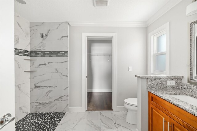 bathroom with vanity, ornamental molding, toilet, and a tile shower