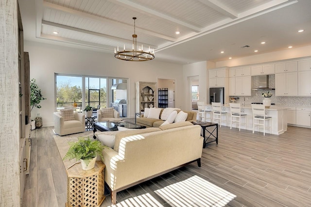 living room with a notable chandelier, beamed ceiling, and light wood-type flooring