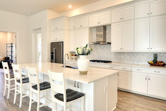 kitchen featuring high quality fridge, wall chimney exhaust hood, sink, and a kitchen island with sink