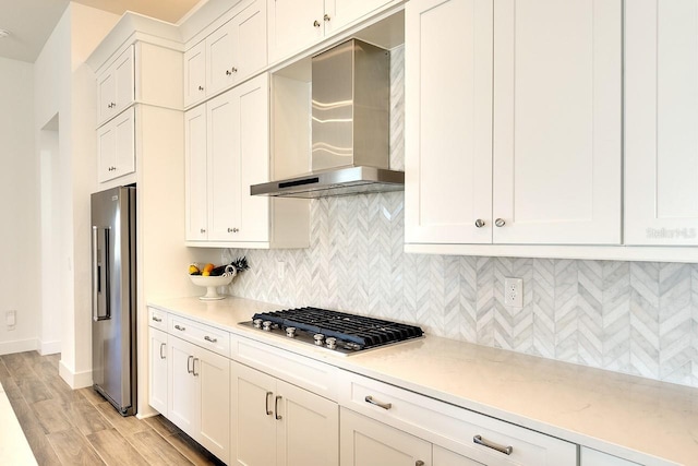 kitchen with wall chimney range hood, backsplash, stainless steel appliances, and white cabinets