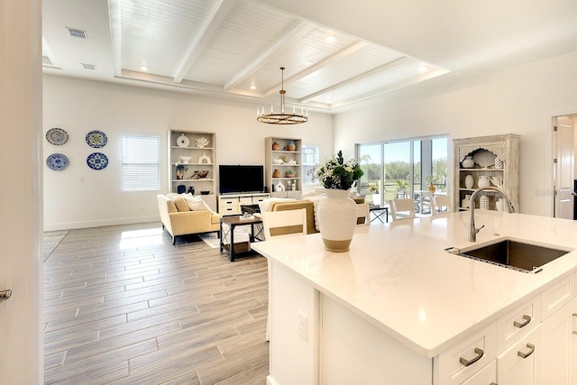 kitchen featuring pendant lighting, white cabinetry, sink, light stone countertops, and a center island with sink