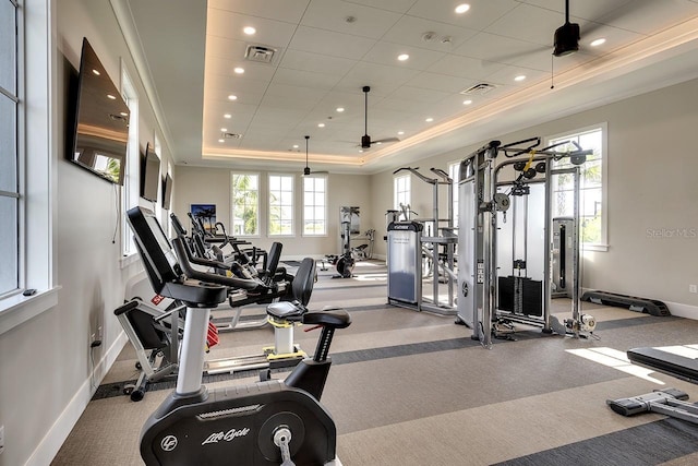 exercise room featuring ceiling fan, ornamental molding, a raised ceiling, and a healthy amount of sunlight