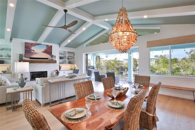 dining room featuring ceiling fan with notable chandelier, a fireplace, beamed ceiling, light wood-type flooring, and built in shelves