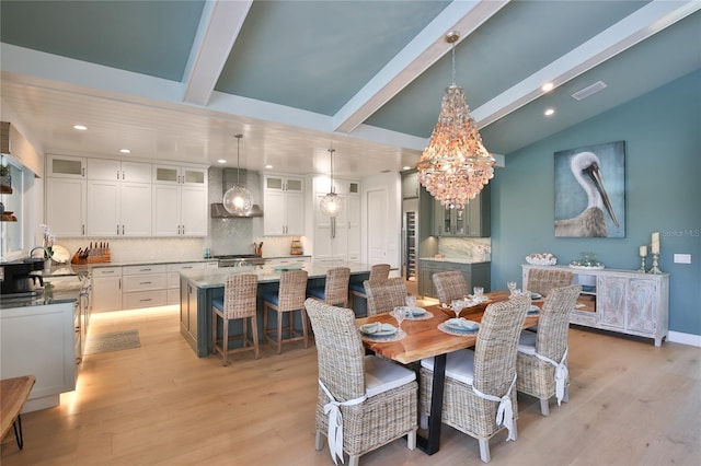 dining room with lofted ceiling with beams, sink, an inviting chandelier, and light hardwood / wood-style floors