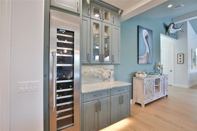 bar featuring light stone counters, vaulted ceiling, beverage cooler, light hardwood / wood-style floors, and decorative backsplash