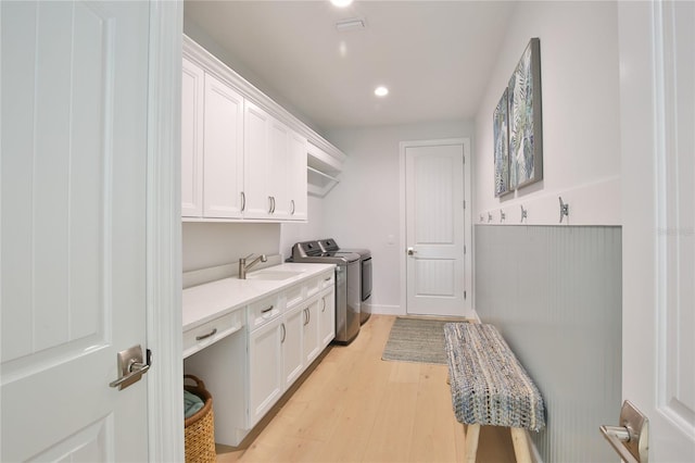 clothes washing area with washer and dryer, sink, light hardwood / wood-style flooring, and cabinets