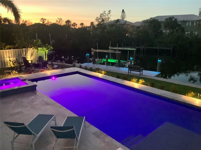 pool at dusk featuring an in ground hot tub and a patio