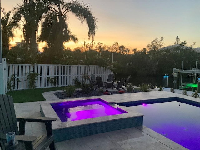 pool at dusk featuring a patio area and an in ground hot tub