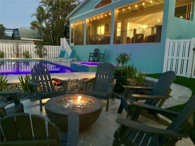 patio terrace at dusk featuring a fenced in pool and a fire pit