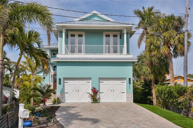 beach home featuring a standing seam roof, decorative driveway, an attached garage, metal roof, and a balcony