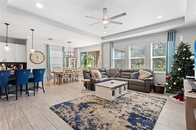 living room featuring a raised ceiling, plenty of natural light, and ceiling fan