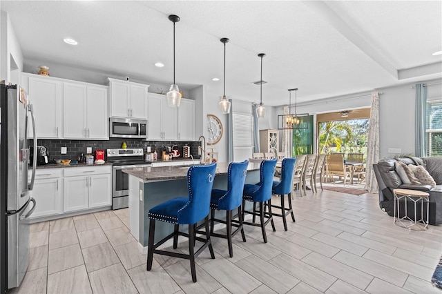 kitchen with pendant lighting, appliances with stainless steel finishes, a kitchen breakfast bar, an island with sink, and white cabinets