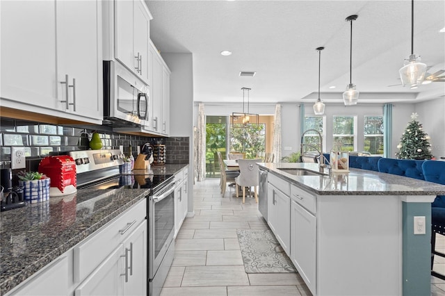 kitchen with pendant lighting, sink, stainless steel appliances, white cabinets, and a center island with sink